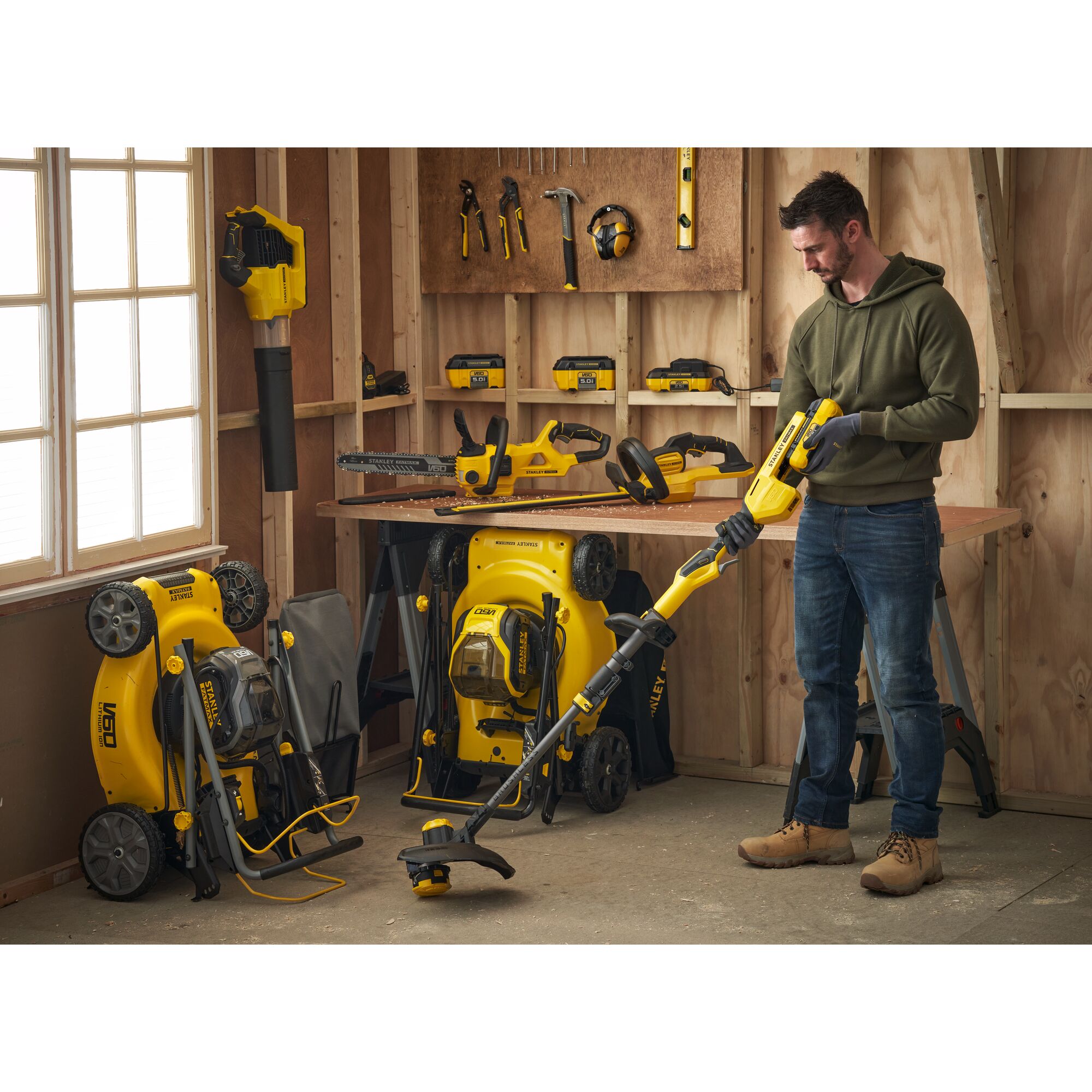 STANLEY SFMCBLB76B blower in use, surrounded by yellow STANLEY tools and lawn mowers in a workshop setting.